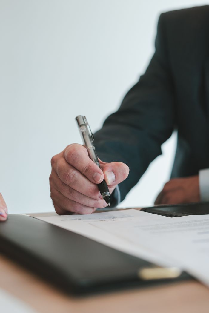 Наши услуги A businessman in a suit signing a contract in an office setting, emphasizing professional context.