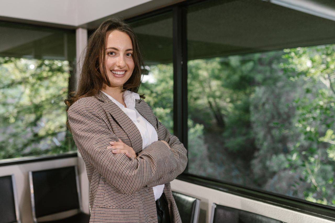Наши услуги Portrait of a smiling businesswoman in an office with large windows.