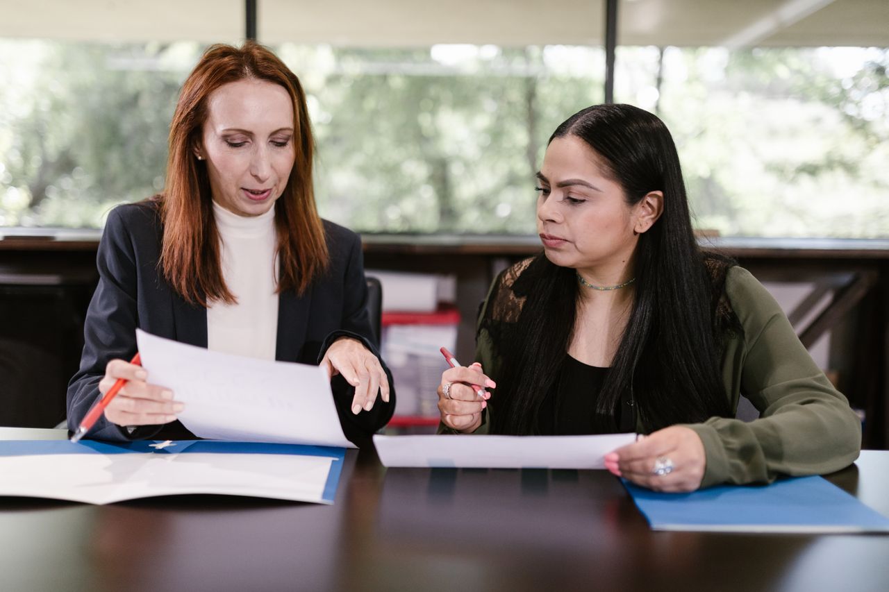 Home Two professional women reviewing documents in a well-lit office setting.